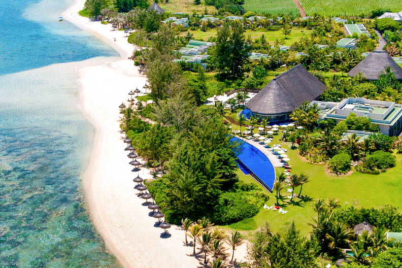 Piaszczysta plaża z parasolami, turkusowa woda i zielony kurort widziane z góry.