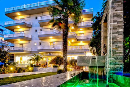 Hotel nocą. Na pierwszym planie palma i fontanna.
