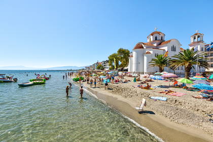 Plaża w Grecji z kościołem w tle. Widoczne parasole i ludzie.