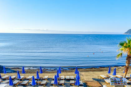 Widok z góry na plażę i taras hotelowy z leżakami oraz stolikami.