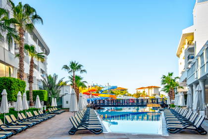 Basen hotelowy z leżakami i palmami. W tle widać zjeżdżalnie.