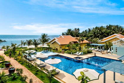 Hotel z basenami, palmami i plażą w tle.