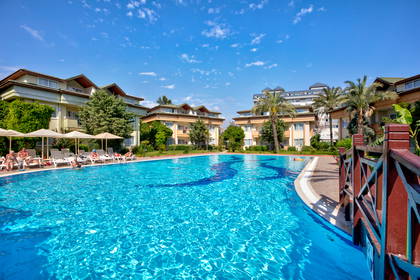 Kompleks hotelowy z basenem i leżakami w słoneczny dzień.