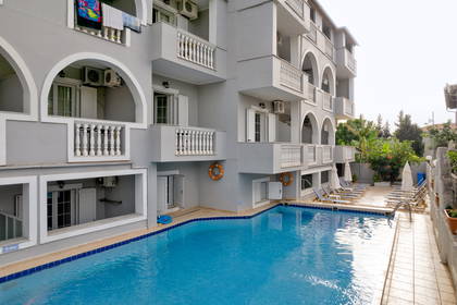 Basen hotelowy z leżakami i budynkiem w tle.