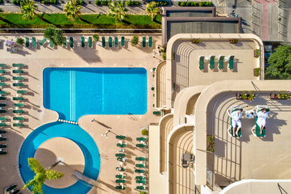 Hotel z basenem, leżakami i palmami, widok z góry.