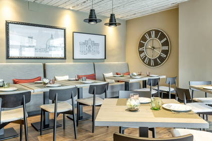 Restauracja z nakrytymi stołami, rysunkami na ścianach i dużym zegarem.