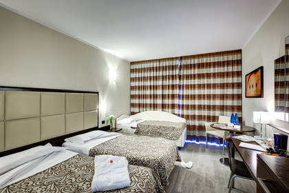 Pokój hotelowy z trzema łóżkami, biurkiem i zasłonami w paski.