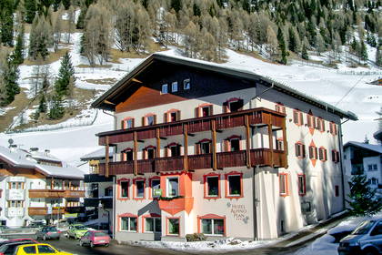 Hotel w zimowej scenerii górskiej, w tle zalesione wzgórza.