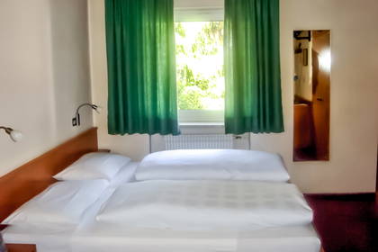 Pokój hotelowy z pojedynczym łóżkiem i zielonymi zasłonami.