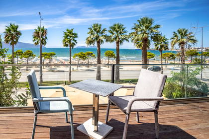 Krzesła i stolik na tarasie z widokiem na plażę i palmy.