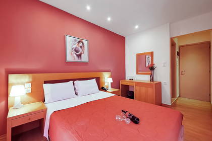 Pokój hotelowy z czerwonymi ścianami, łóżkiem oraz winem i kieliszkami.