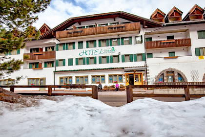 Hotel Orsa Maggiore z białymi ścianami i zielonymi okiennicami, otulony śniegiem.