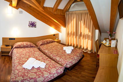 Pokój hotelowy na poddaszu z dwoma łóżkami i drewnianymi elementami.