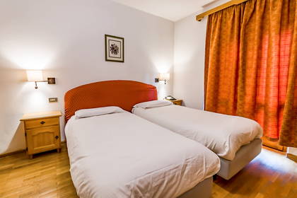 Pokój hotelowy z dwoma łóżkami, stolikiem nocnym i pomarańczowymi zasłonami.