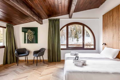 Pokój hotelowy z dwoma łóżkami, drewnianym sufitem i widokiem na zaśnieżony las.