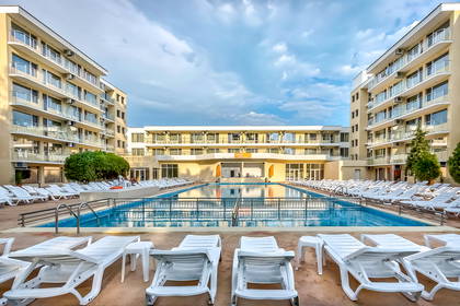Basen z leżakami otoczony budynkami hotelowymi.