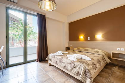 Pokój hotelowy z łóżkiem, balkonem i elementami wystroju w brązach.