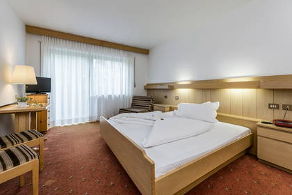 Jasny pokój hotelowy. Drewniane meble, duże łóżko i okno.