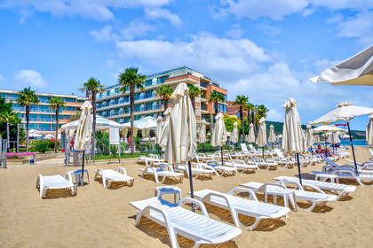 Plaża z białymi leżakami i parasolami. W tle hotel i palmy.
