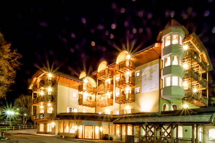 Oświetlony hotel nocą z balkonami i wieżą.