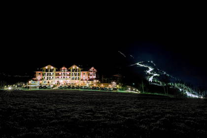 Oświetlony hotel i stok narciarski nocą.