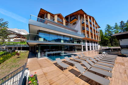 Hotel z basenem i leżakami na tle gór.