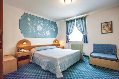 Pokój hotelowy z łóżkiem, fotelem i niebieską wykładziną.