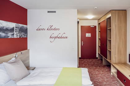 Pokój hotelowy z łóżkiem, szafą i czerwonymi dodatkami.