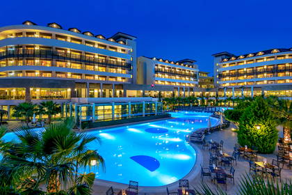 Hotel z basenem i palmami oświetlony nocą (panorama).