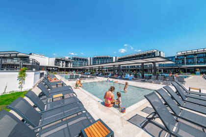 Basen hotelowy z leżakami, wypełniony ludźmi w słoneczny dzień.