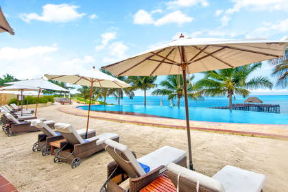 Leżaki i parasole na plaży przy basenie typu infinity pool.