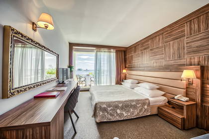 Pokój hotelowy z łóżkiem, biurkiem i balkonem z widokiem na morze.