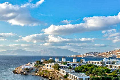 Mykonos: wiatraki, morze i zabudowa miejska na tle błękitnego nieba.