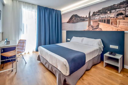 Pokój hotelowy z łóżkiem, biurkiem i fototapetą.