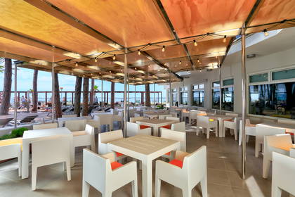 Restauracja z widokiem na plażę. Lokal ma białe meble i zadaszenie.