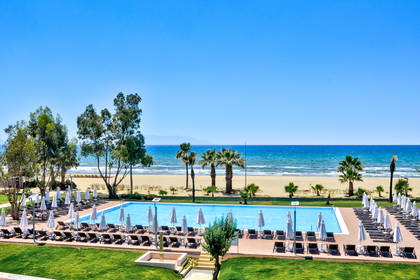 Basen z leżakami, plażą i palmami.