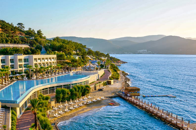 Luksusowy kurort nad morzem z basenem bez krawędzi i drewnianym molo.