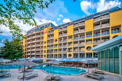 Żółty hotel z basenem i leżakami.