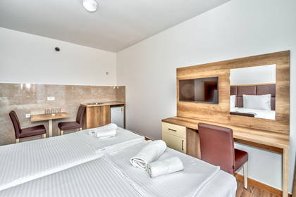 Jasny pokój hotelowy z dwoma łóżkami, telewizorem i aneksem kuchennym.