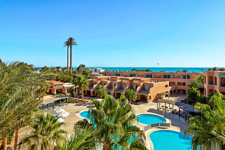 Kompleks hotelowy z basenami i palmami w słoneczny dzień.