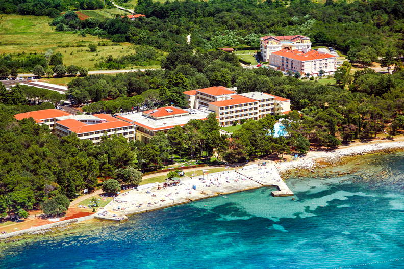 Widok z lotu ptaka na otoczony lasem kompleks hotelowy przy plaży nad turkusowym morzem.
