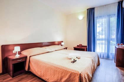 Pokój hotelowy z łóżkiem, szafkami nocnymi i zasłonami w oknach.