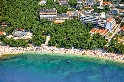 Zatłoczona plaża w Chorwacji z lotu ptaka. Wokół zielone drzewa i hotele.
