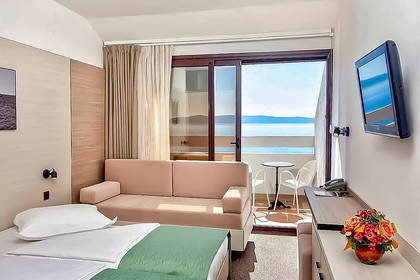 Pokój hotelowy z łóżkiem, sofą i balkonem z widokiem na morze.