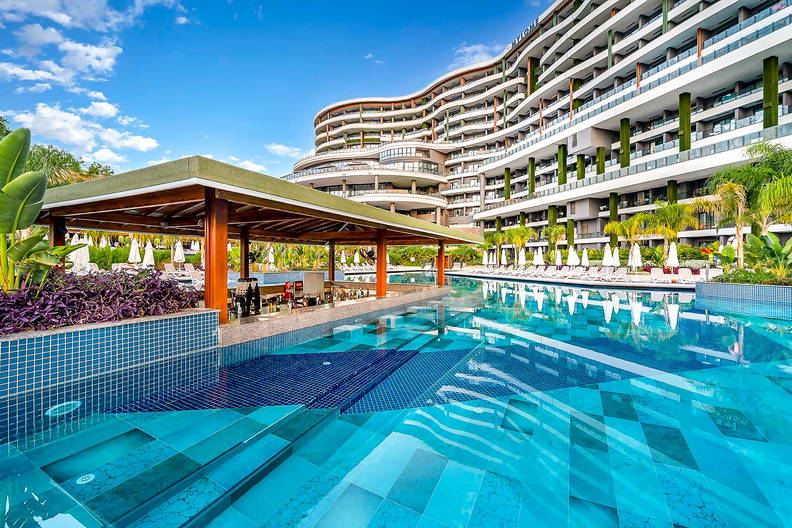 Basen hotelowy z barem i leżakami. W tle budynek.