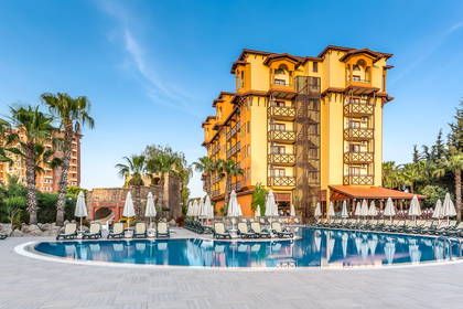 Hotel z basenem, leżakami i palmami w słoneczny dzień.