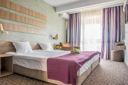 Pokój hotelowy z dużym łóżkiem, fotelem i fioletowymi zasłonami w oknie.