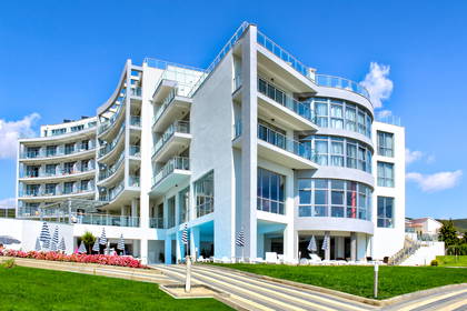 Nowoczesny, biały hotel z balkonami i niebieskimi parasolami.