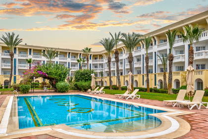 Basen z leżakami i palmami przy hotelu.