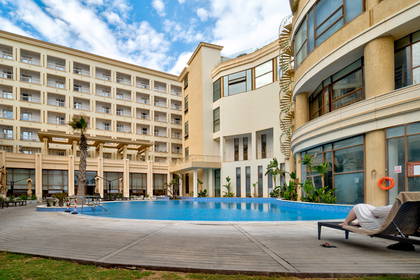 Kompleks hotelowy z basenem. Osoba odpoczywa na leżaku.